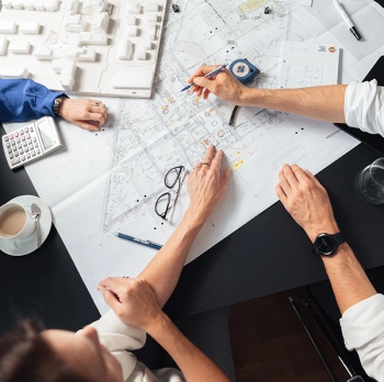 MitarbeiterInnen von Swietelsky arbeiten, gebeugt über einem Grundrissplan und Gebäudemodell